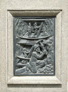 Laxey Great Mine memorial carving to miners showing men hacking at coal deep below ground. 