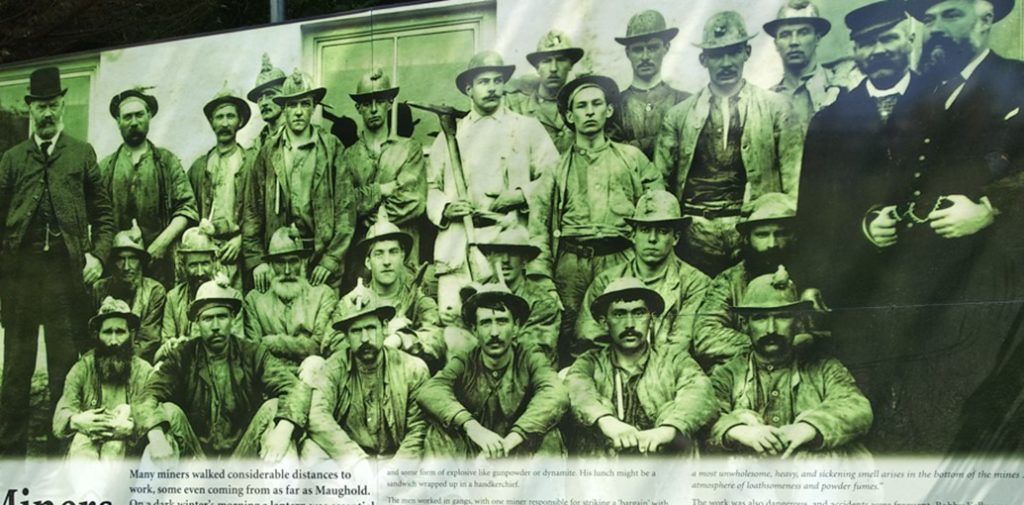 Photo of the billboard with the miners of Laxey showing three rows of miners in black and white