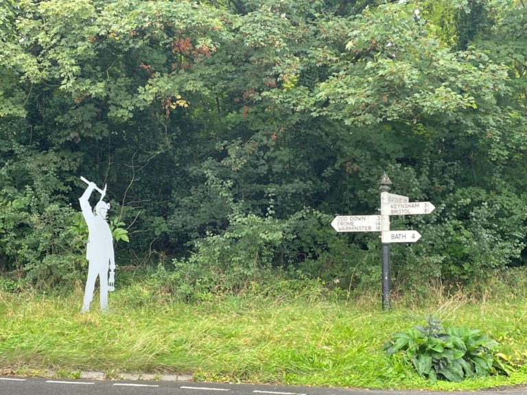 Somerset metal coal mining silhouette of a 2m high miner with raised pitchfork at Newton St Loe next to a signpost showing directions to Bristol and Bath.